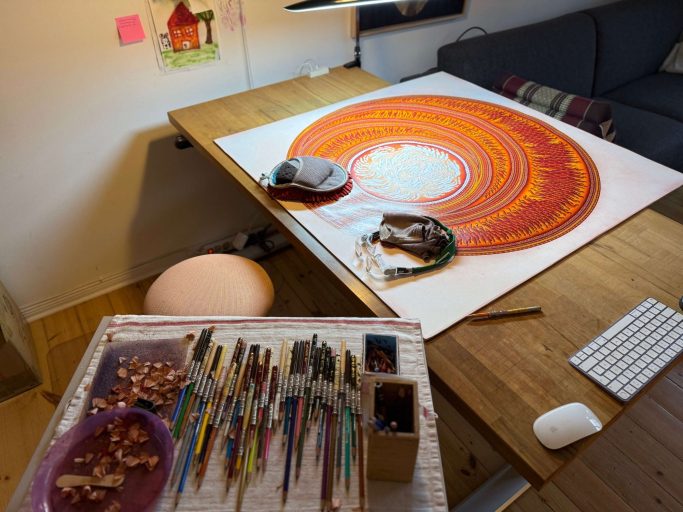 Ein kreativer Arbeitsplatz mit bunten Malutensilien und einem spiralförmigen Kunstwerk.